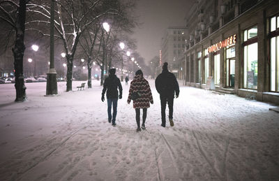 Rear view of people walking on snow in city