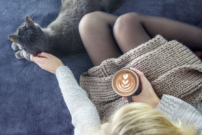 Directly above shot of woman holding coffee while stroking cat on carpet