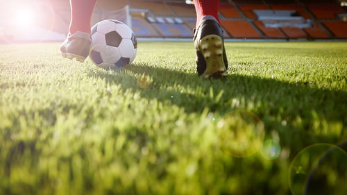 Low section of man playing soccer at stadium on sunny day