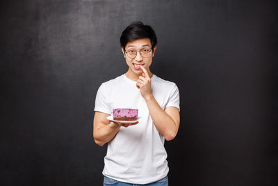 Young man with cake against black background