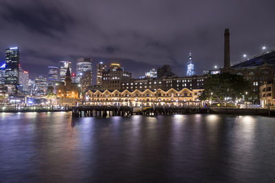 Illuminated buildings by river against sky at night