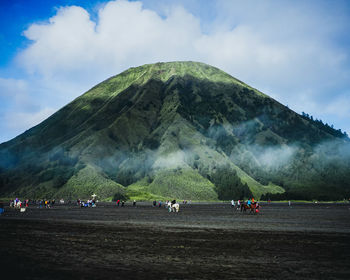 Distant view of tourists on field against volcano