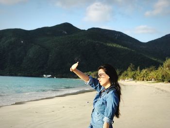 Young woman standing on beach against sky