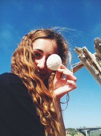 Low angle portrait of young woman holding sand dollar in front of eye