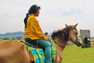 Senior woman riding horse against sky