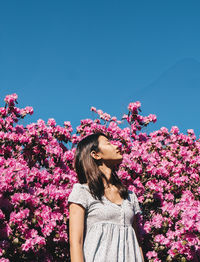 Beautiful woman standing by pink flowering plants against sky