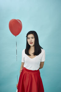 Portrait of woman holding heart shape balloon against blue background