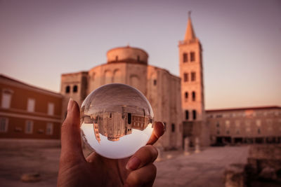 Midsection of person holding photo ball against buildings in city