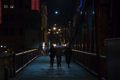 Rear view of men walking on illuminated city at night