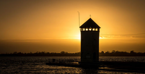 Silhouette of lighthouse at seaside during sunset