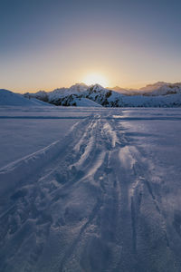 Snow covered landscape against sky during sunset