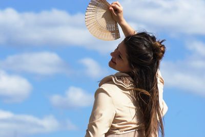 Woman with paper fan posing against blue sky