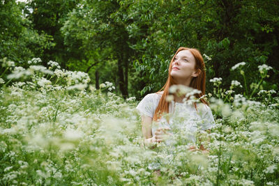 Woman standing by flower plants against trees