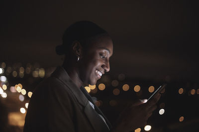 Smiling businesswoman text messaging on mobile phone at night