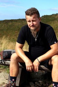 Young man sitting on field against sky