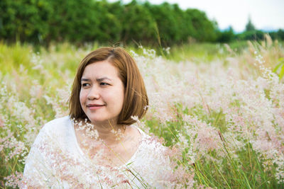 Smiling woman looking away amidst flowers on field