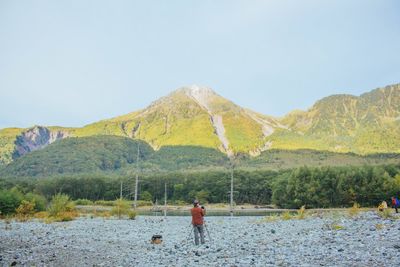 Rear view of man standing on mountain by lake against clear sky
