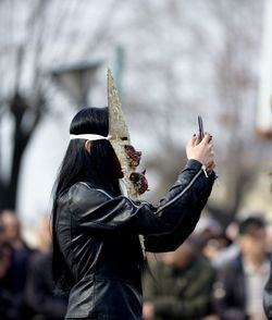 Side view of woman taking selfie while wearing mask at carnival