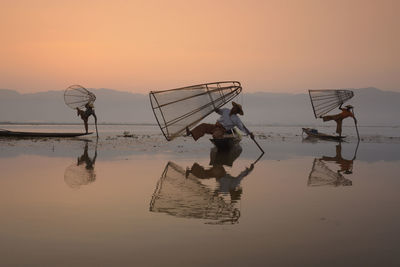 Fishermen fishing in lake against sky during sunset