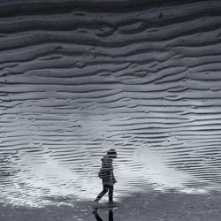 Reflection of woman walking on wet sandy beach