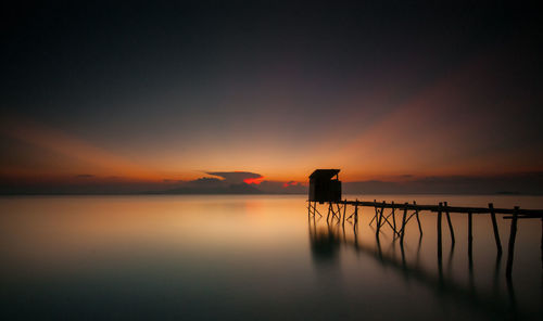 Silhouette of jetty over river at dusk