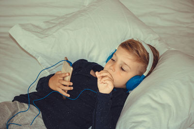 Cute boy listening to music while resting on bed