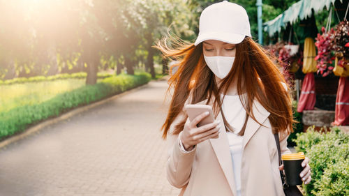Redhead woman wearing face mask for virus protection. young business woman with cell phone in hand