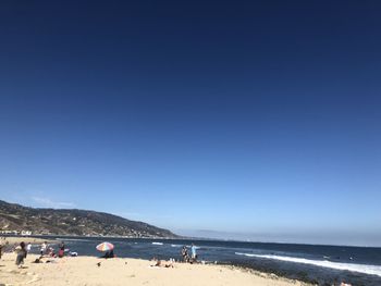 Group of people on beach against clear blue sky