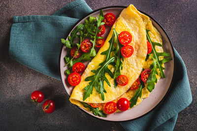 Close up of french omelette filled with cherry tomatoes and arugula on a plate on the table top view