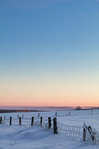 Scenic view of snow covered field against clear sky during sunset