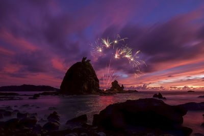 Firework display over sea against sky during sunset