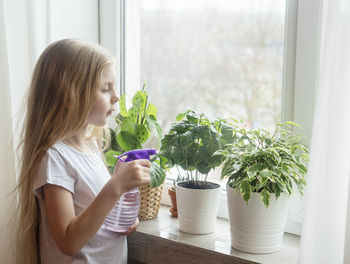 Girl spraying water on plant at home