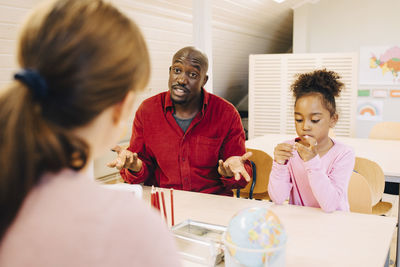 Surprised man sitting with son talking to teacher at classroom