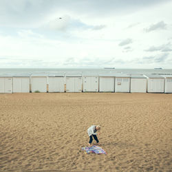 Rear view of child standing on beach against sky