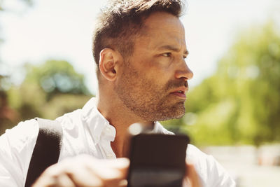 Thoughtful businessman holding smart phone on sunny day