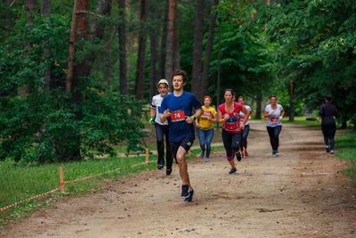 People running on road amidst trees in forest