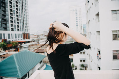 Side view of young woman standing on building terrace against sky