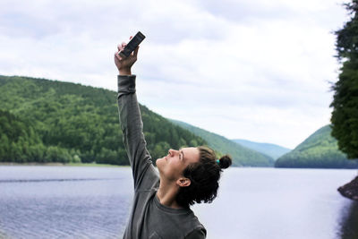 Rear view of woman with arms raised against lake