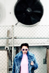 Portrait of woman wearing sunglasses against chainlink fence