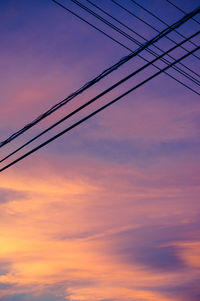 Low angle view of power lines against orange sky