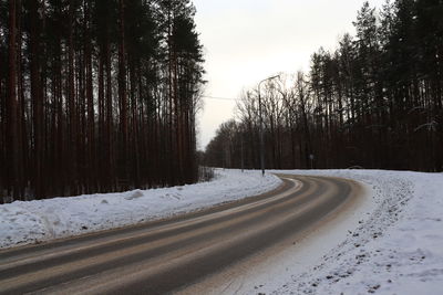 Snow covered road amidst trees against sky