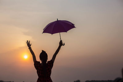 Silhouette people holding purple tree against sky during sunset