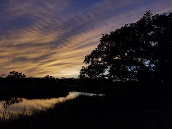 Silhouette trees by lake against sky during sunset