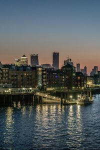 Illuminated buildings by river against sky at dusk