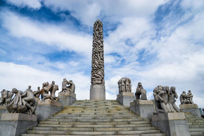 Low angle view of sculptures at gustav vigeland sculpture park against cloudy sky