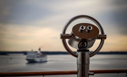 Coin-operated binoculars by sea against sky during sunset