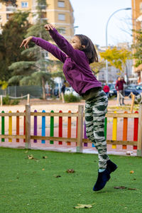 Side view of girl with arms raised jumping in park