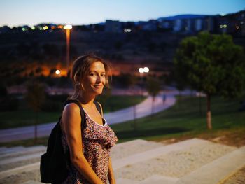 Portrait of smiling woman standing in city at sunset