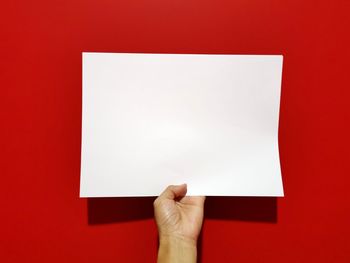 Low section of person holding paper against red background