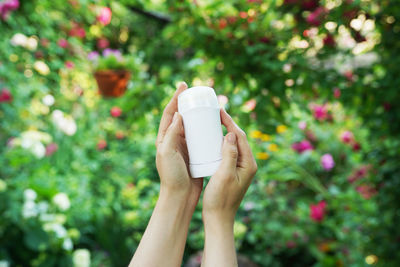 Hands holding natural deodorant on green flowers background. zero waste concept
